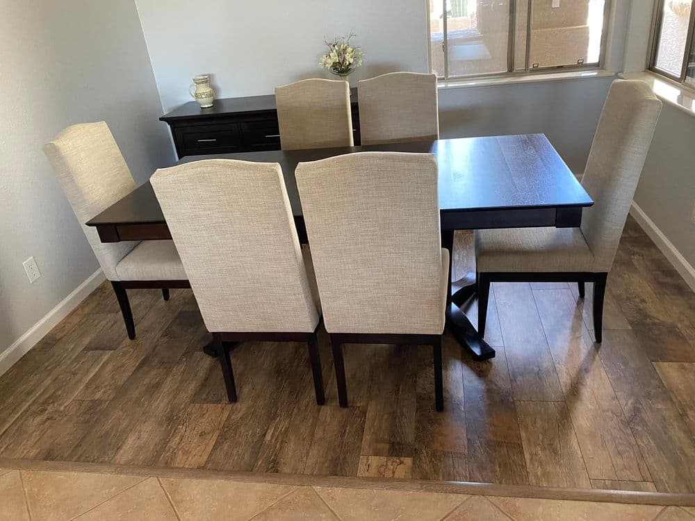 Modern dining room setup with a wooden table and six upholstered chairs on wood and tile flooring.