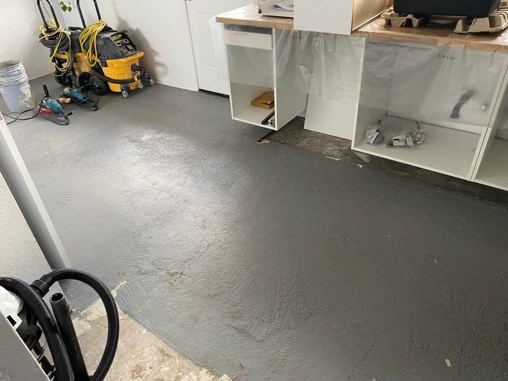 unfinished garage floor with gray epoxy coating and construction tools in the background