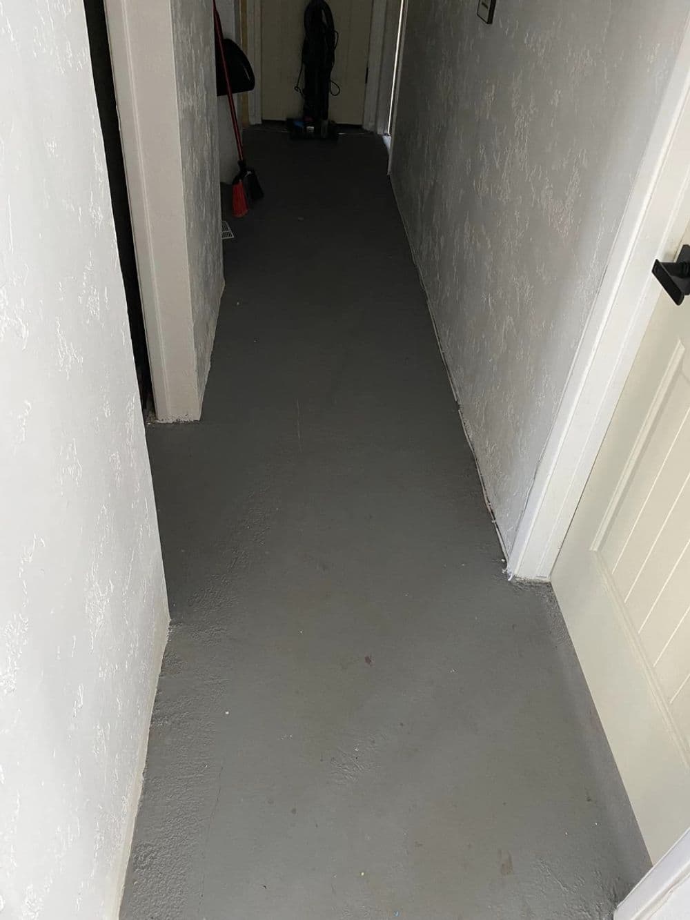 Narrow gray hallway with textured walls and a closed door at the end.