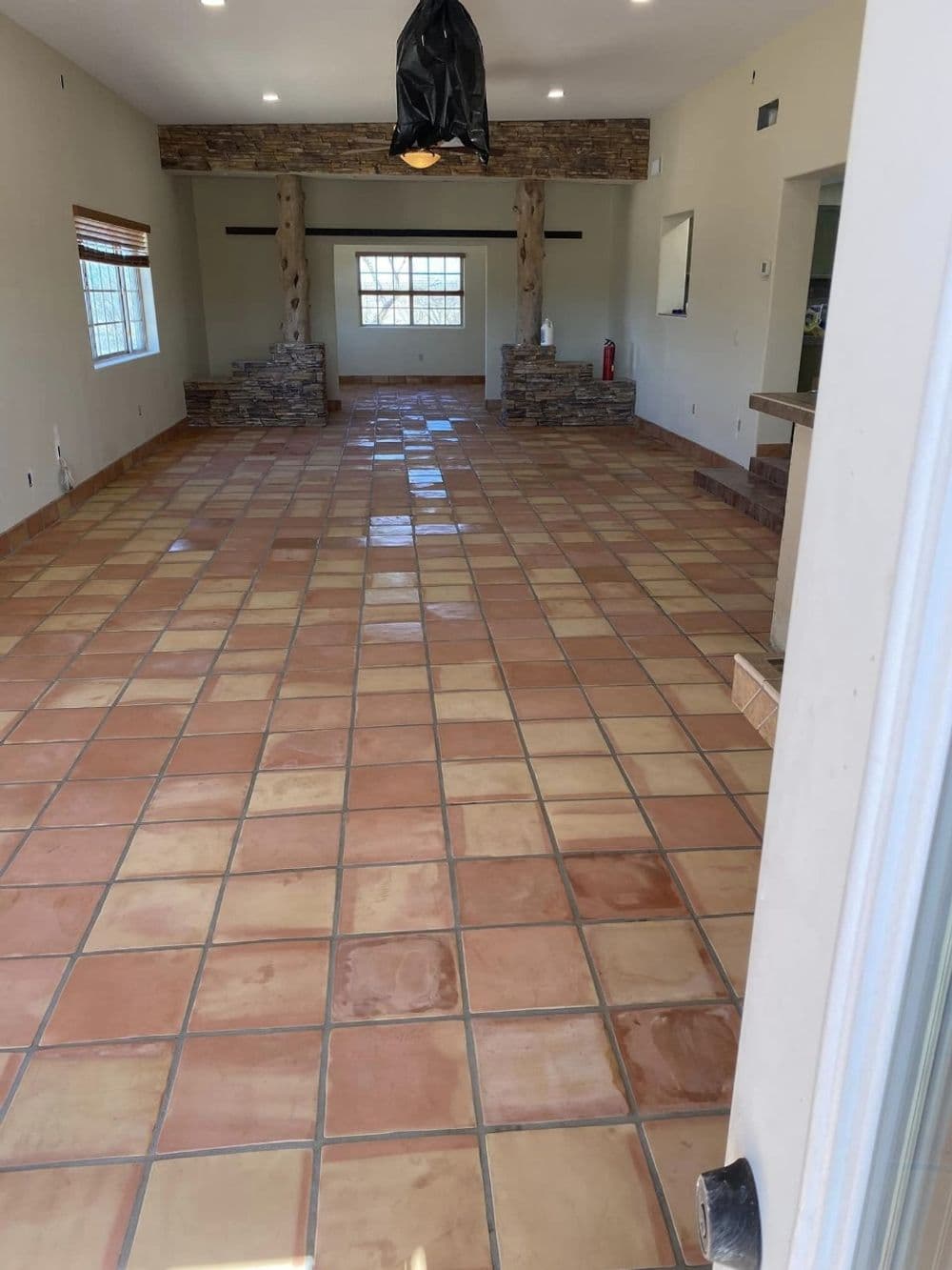 Spacious room with terra cotta tile floor and stone pillars, featuring natural light from windows.