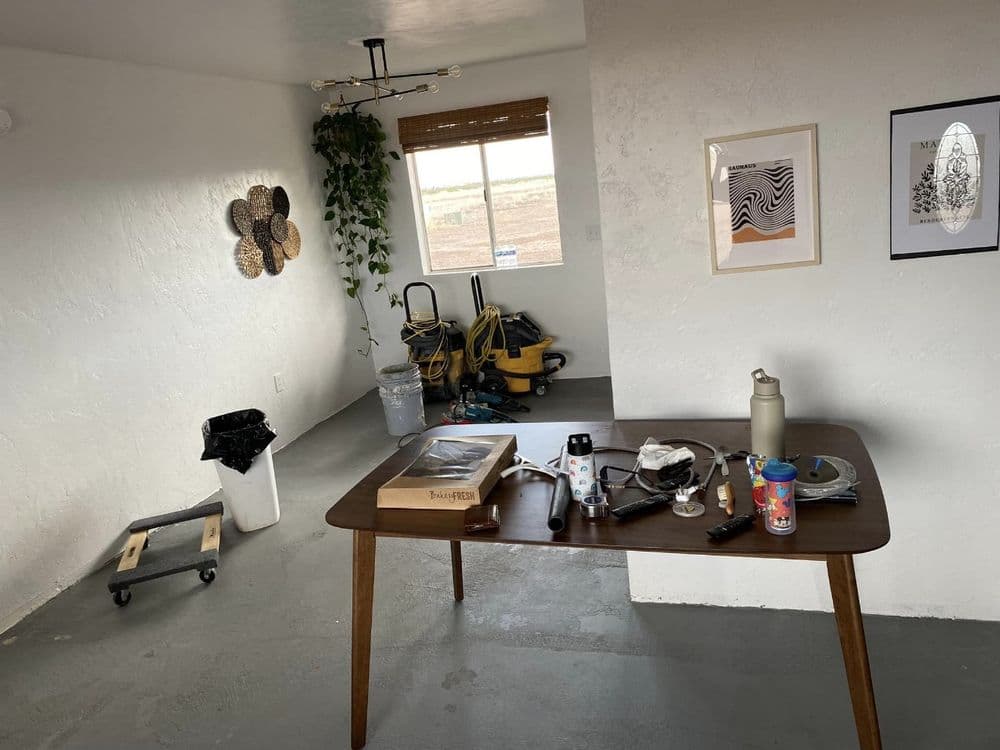 Home office with a wooden table, tools, decor, and a large window overlooking a field.