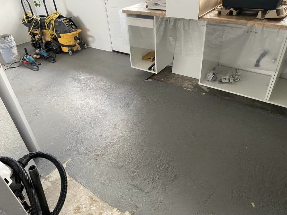 Renovated garage floor with fresh gray coating, tools and supplies in the background.