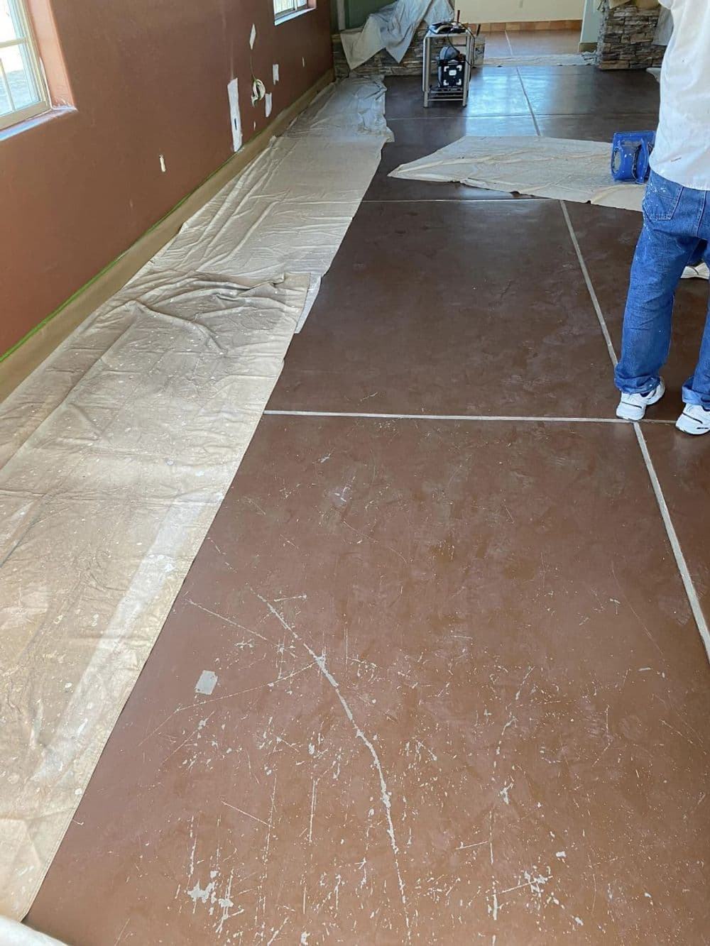 Brown concrete floor preparation with painter's tarp and tools in a room renovation setting.